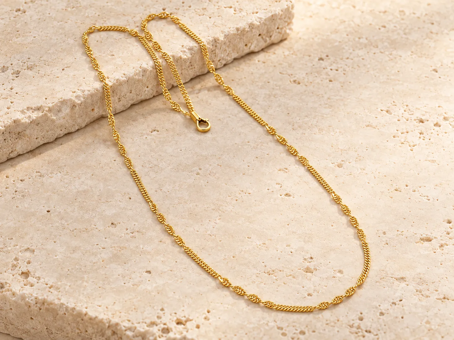 Gold chain necklace with alternating link sections, draped over a stone ledge