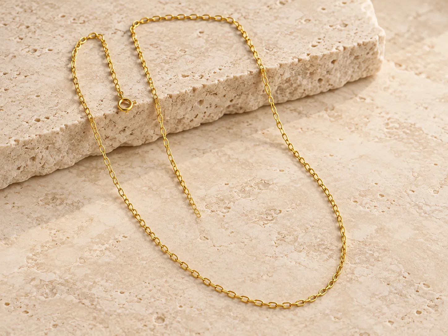 Gold long-link chain necklace on a warm stone surface