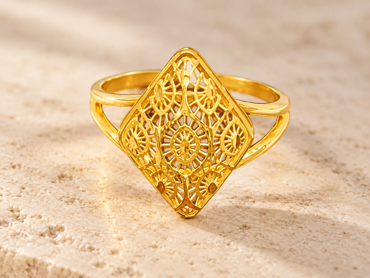 Gold ring with a diamond-shaped filigree front, resting on pale stone