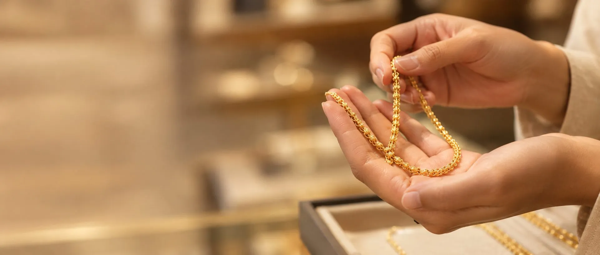 Hands holding a gold chain above a jewellery display tray